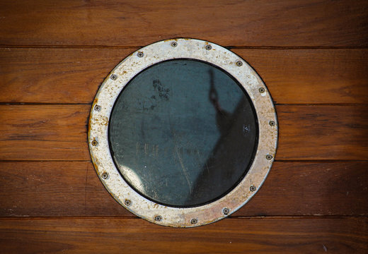 Rusty old iron round window porthole on the old wood wall background.
