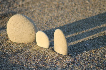 Fototapeta na wymiar Three pebbles in a row on the sunset beach. Diagonal shadows.