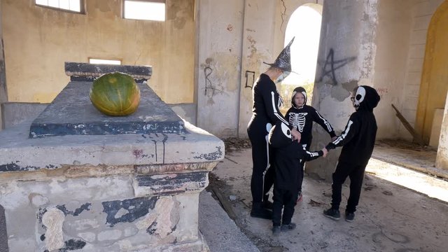 Children and their mother in carnival costumes celebrate Halloween in cult place Mortuary or Pantheon. Ancient ruined building. Rituals of Samhain, All Hallows' Eve, festival of dead. Parentalia