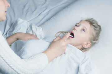 a girl with white hair lies in bed. mom using an inhaler makes an injection in the throat of a patient.