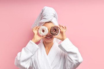 Smiling beautiful woman after bathing posing with donuts in pink isolated studio. Portrait of...