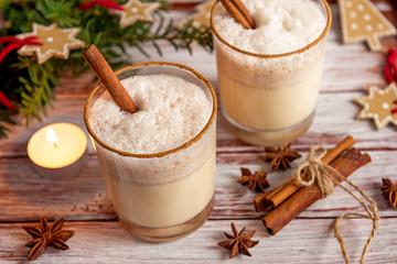 Eggnog in glass cups with a delicate foam, spices and a cinnamon stick