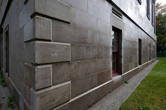 The corner view of a large stone government courthouse. The old marble building is grey with multiple windows on both exterior sides. Grass is on the ground and trees in the background.  