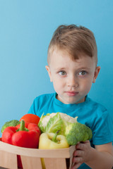 Boy holding basket with fresh vegetables on blue background. Vegan and healthy concept.