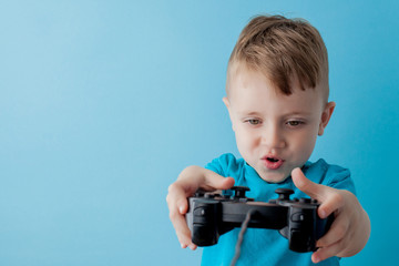 Little kid boy 2-3 years old wearing blue clothes hold in hand joystick for gameson blue background children studio portrait. People childhood lifestyle concept. Mock up copy space