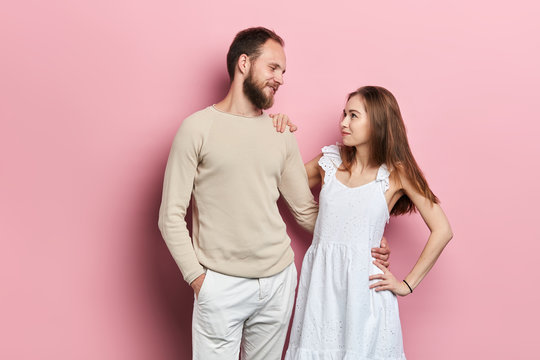 young woman and man in cassual clothes looking at each other, love tender feeling. close up portrait, isolated pink bacakground, family tire, relatonship between wifee and husband
