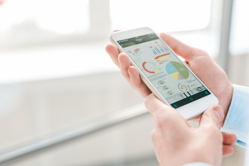 Young economist or financial analyst holding smartphone with charts and diagrams