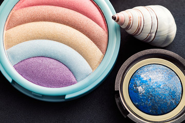The eyeshadow palette and makeup brushes, blush and iridescent decoration against a dark background