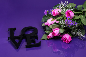 Bouquet of pink roses sitting next to a black love sign with text space