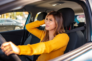 Young businesswoman driving a car while being tired from work. Distraught mid adult woman driving a car. Displeased young stressed angry pissed off woman driving car annoyed by heavy traffic