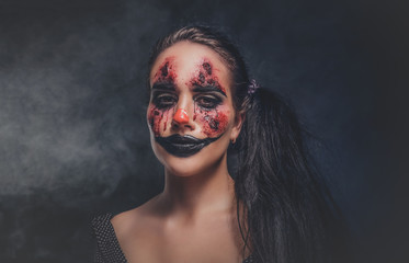 In smoky dark photo studio woman in a role of evil clown is posing for photographer.