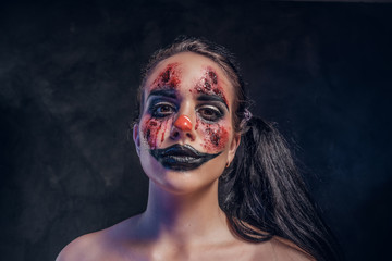 In smoky dark photo studio woman in a role of evil clown is posing for photographer.