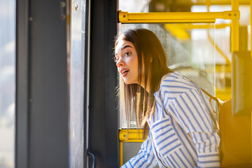 Young woman in a public transport. A young pretty woman standing in a bus. Young adorable joyful woman is standing on the bus.