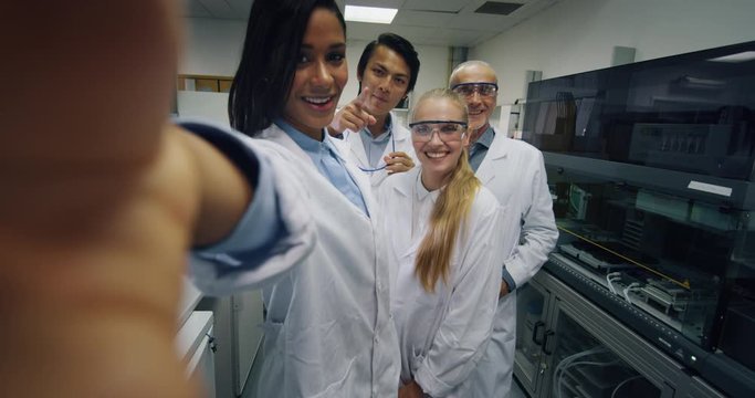 A group of scientists with protective glasses are making a video call to colleagues or selfie satisfied with great results of completed research in a laboratory. 
