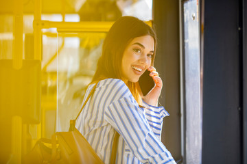 The passenger use smartphone in the bus or train, traveling concept.  Woman is standing on the bus using the phone and smiling. Smiling Woman Talking On Phone in Bus.
