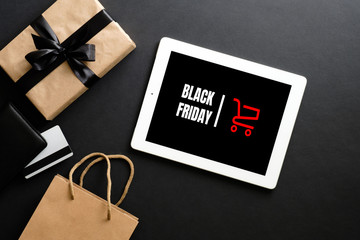 Black Friday sale concept. Tablet pad with sign "Black Friday" on screen, shopping bag, gift box over black background. Flat lay, top view, overhead. - Powered by Adobe