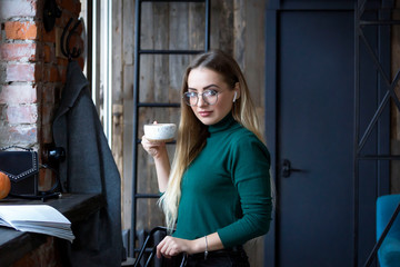 Obraz na płótnie Canvas Young beautiful blonde in glasses sits in a cafe on the street and in the inside.