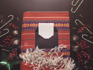 A blank sheet of paper is in a black envelope on a colorful fringed plaid. Nearby are various...