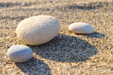 Fototapeta na wymiar Three white pebble stones on the sand. Sunset photo with long shadows.