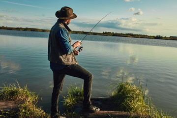 Caucasian adult man stand near blue lake and fish. He shows an himself son how fish.