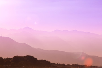 Sea and mountains purple sunset landscape. Haze silhouette.