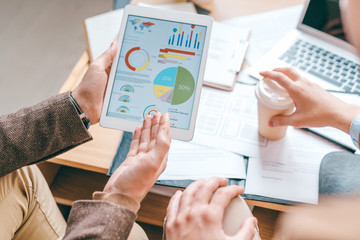 Young male economist with touchpad pointing at financial diagram on screen