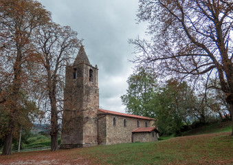 Fototapeta na wymiar Autumn trees with brown leaves and ground covered by leaves in the park with old church. North of Spain.