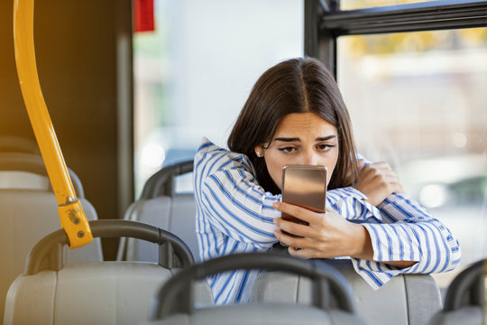 Young sad, upset girl uses a mobile phone in the city bus. Technology cell phone isolation. Internet and social media. Worried woman traveling with public transport, leaning, holding smart phone.