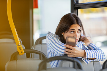 Young sad, upset girl uses a mobile phone in the city bus. Technology cell phone isolation....