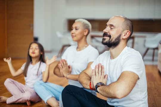 Young caucasian parents with child meditating at home isolated in room , sitting on floor. Family, sport, yoga concept. White colors