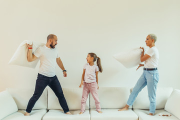 Obraz premium Happy joyful family fighting pillow battle on bed at home with children. Parents have pillow fight with daughter. Positive family, laughing. Friendly family