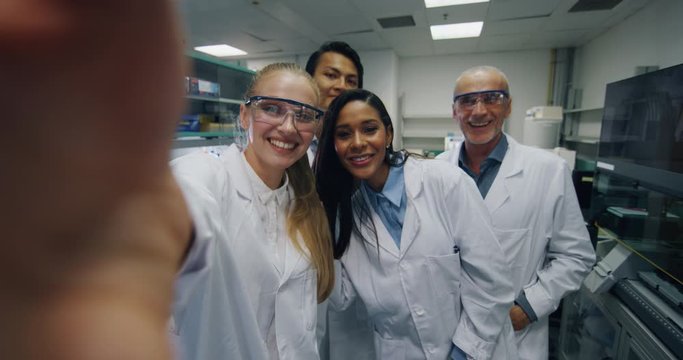 A group of scientists with protective glasses are making a video call to colleagues or selfie satisfied with great results of completed research in a laboratory. 