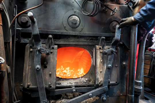 An open door to the furnace of a steam engine. Coal burns in the furnace, an orange flame is visible. The interior is inside a steam locomotive, there is metal fittings. Background. Texture.