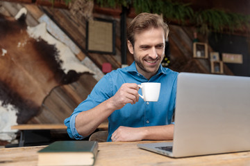 Joyful casual man reading, laughing, and drinking his coffee