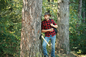 Naklejka na ściany i meble Stylish young man posing like lumberjack. Harvest of timber. Deforestation. Firewood as a renewable energy source. The Lumberjack working in a forest.