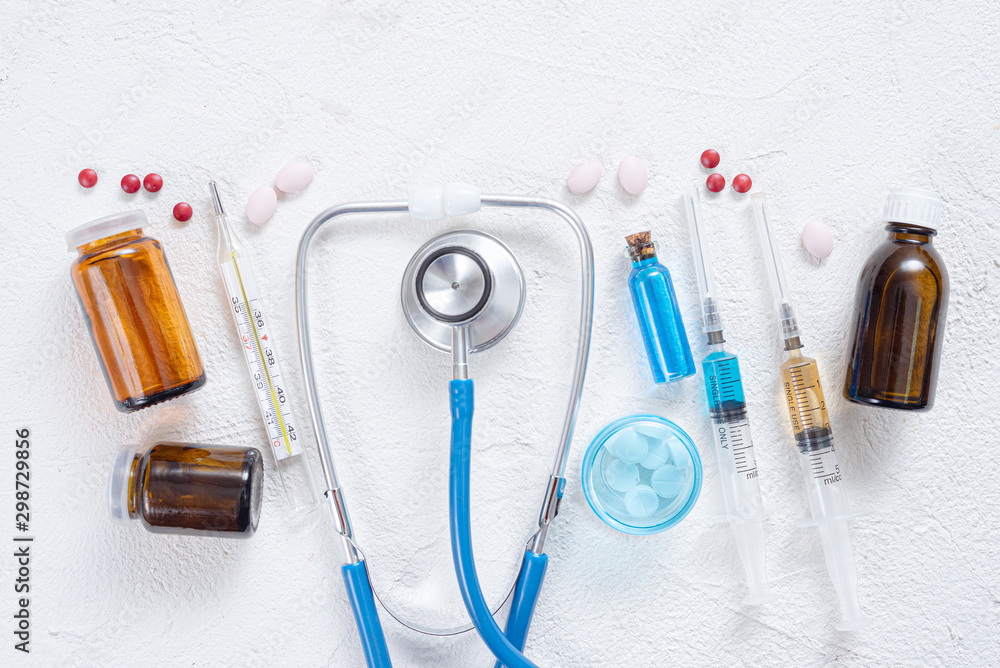 Wall mural Syringe, stethoscope, thermometer, various tablets and bottle with blue liquid on a white background. Medical flat lay background.