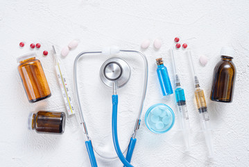Syringe, stethoscope, thermometer, various tablets and bottle with blue liquid on a white background. Medical flat lay background.