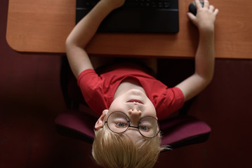 Funny blond boy in glasses resting at a laptop. Internet and preschooler. Top view