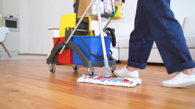 Caucasian woman rolls a cart for floor washing and other equipment for cleaning house. Staff of cleaning service