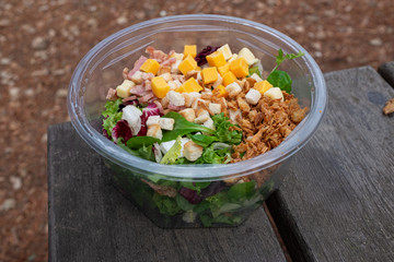 HEALTHY SALAD PLASTIC PACKED ON OLD WOODEN TABLE, DURING FOOD IN THE FIELD