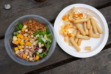  SALAD IN PLASTIC AND CHEESE PLATE CONTAINER ON AGED WOODEN TABLE SEEN FROM ABOVE