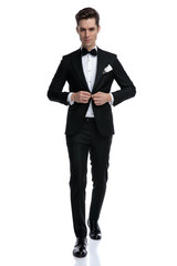elegant young groom walking and fixing coat on white background
