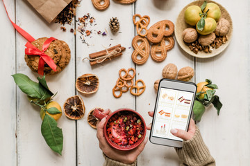 Girl holding drink and smartphone while scrolling through goods in online shop