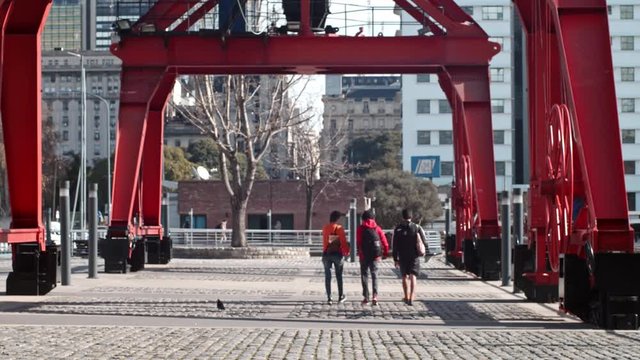 Tres jovenes amigos caminando bajo una gran grùa roja