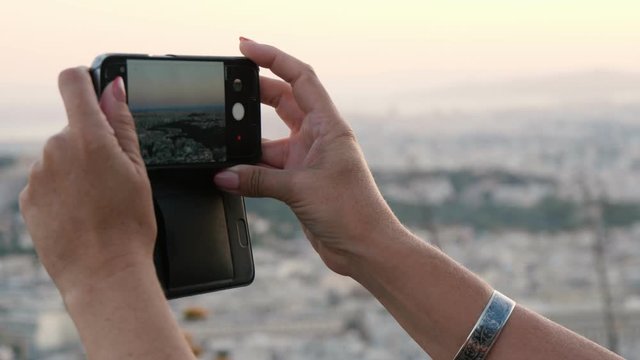 Female hands keeping a smartphone and taking a photo of Athens landscape 