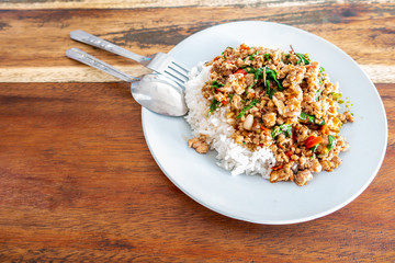 Rice topped with stir-fried pork and basil in  white dish on wooden table. , Text space.