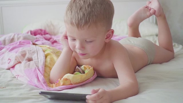 portrite of three year old boy in bed is using a smartphone.