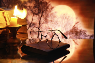 Vintage glasses on an old retro book on a background of the moon. Reading a book by candlelight. The concept of book thrillers and novels.