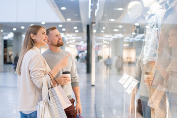 Young woman showing her husband new casualwear collection in shopwindow