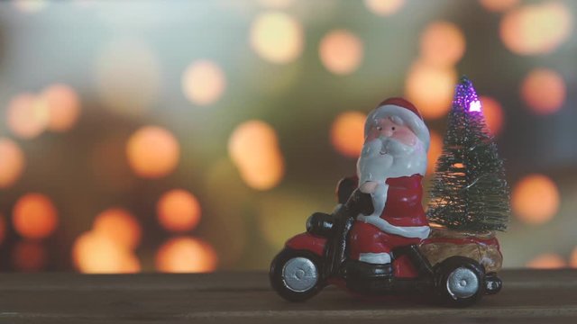 Wooden table with blurred christmas lights bokeh on the background. In the foreground santa claus on a tricycle